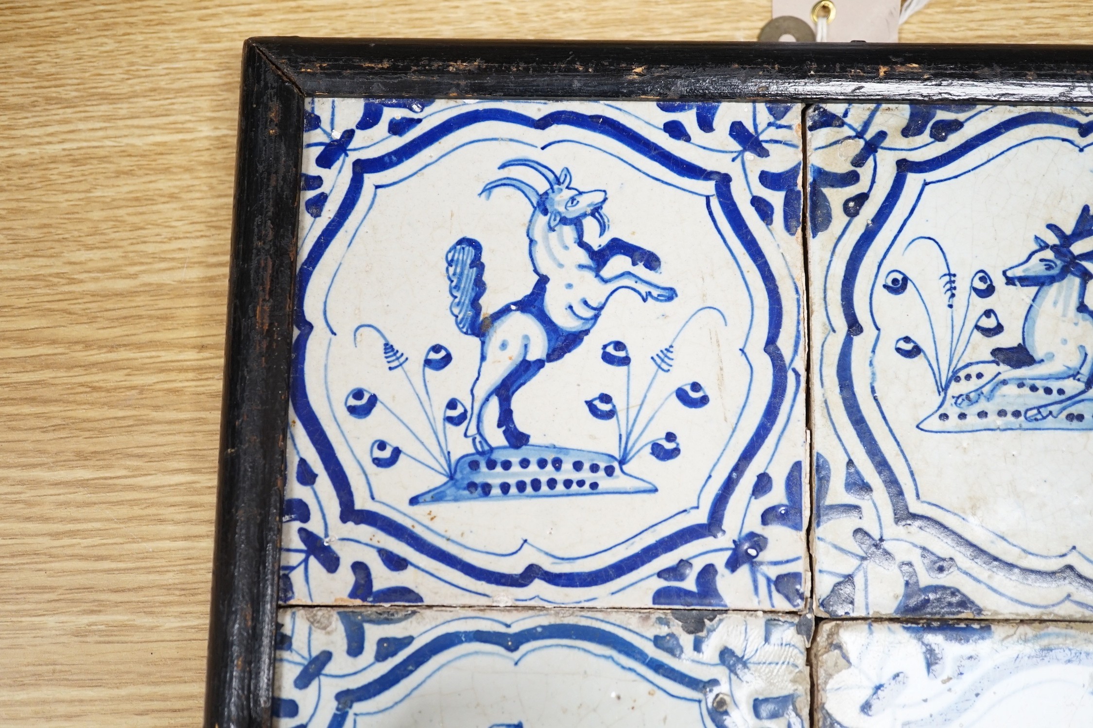 Four 17th century Dutch Delft blue and white tiles, decorated with deer, cockerels and figures within shaped panels (frame 29cm)